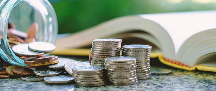 Thomax Immobilier : Pile Of Money Coins In And Outside The Glass Jar On Blurred Book And Natural Green Background For Financial And Education Concept